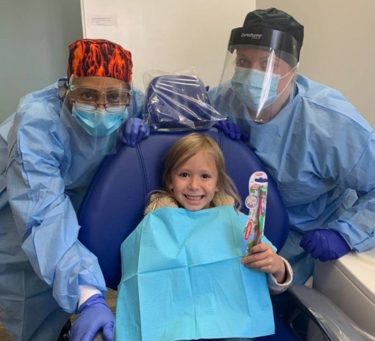 dental volunteers at clinic in us with smiling child in chair holding toothbrush