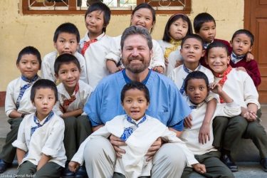 dentist sitting with children for group picture on dental volunteer trip